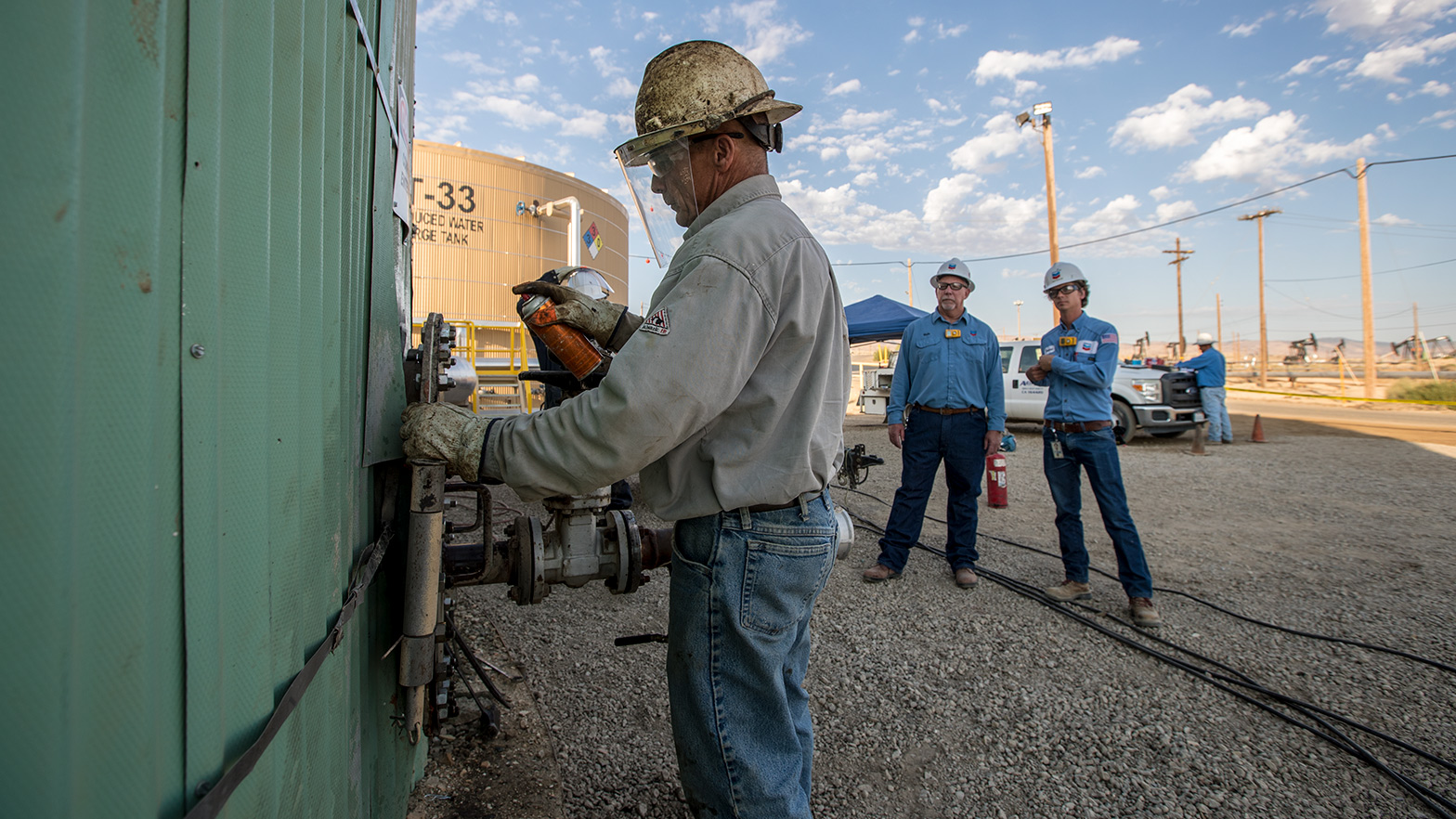 A worker is working on a wheel valve with two other workers looking on at a water recycling plant near the Kern River in the San Joaquin Valley, California.