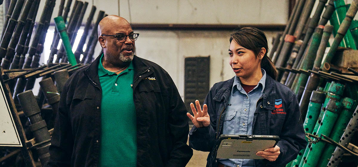 Workers with tablet converse in machine shop.